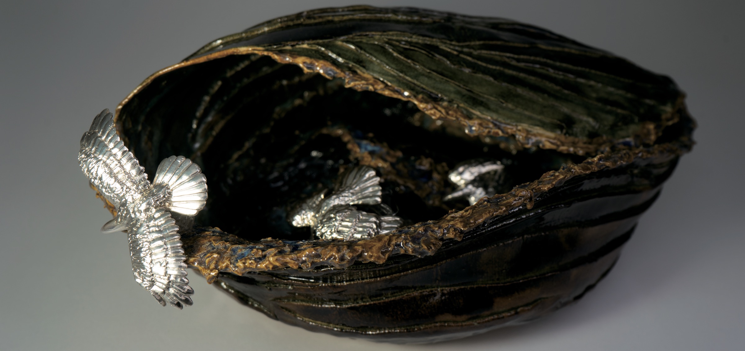 Glazed ceramic vessel holding silver birds in flight.