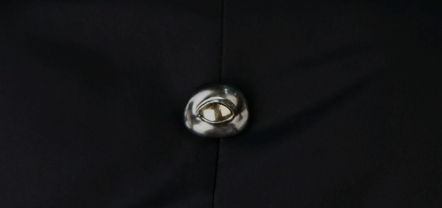 Small silver eye-shaped brooch on black fabric.
